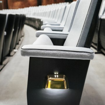 Several rows of modern, upholstered theatre seats in the auditorium of Oper Köln at Offenbachplatz, arranged in perspective. In the foreground, a seat with armrests and the subtly illuminated seat number 11 is visible, while the rows continue into the background, creating a calm and elegant atmosphere.