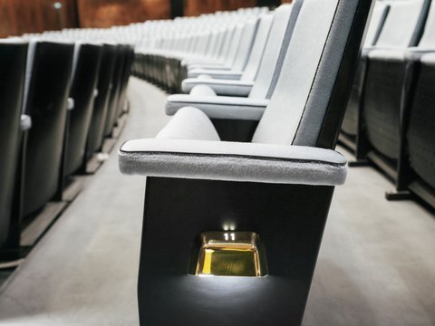 Several rows of modern, upholstered theatre seats in the auditorium of Oper Köln at Offenbachplatz, arranged in perspective. In the foreground, a seat with armrests and the subtly illuminated seat number 11 is visible, while the rows continue into the background, creating a calm and elegant atmosphere.