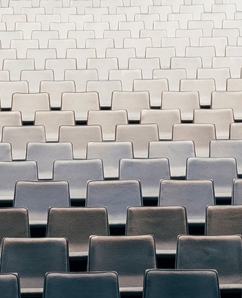 Blick auf zahlreiche, gleichmäßig angeordnete Sitzreihen im Zuschauerraum der Oper Köln am Offenbachplatz. Die hell gepolsterten Sitze bilden ein ruhiges, geometrisches Muster und vermitteln die Größe und Ordnung des Saals, während keine Personen anwesend sind.
