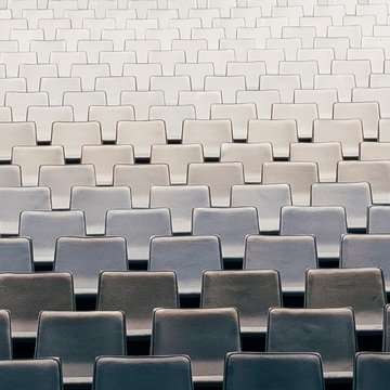 Blick auf zahlreiche, gleichmäßig angeordnete Sitzreihen im Zuschauerraum der Oper Köln am Offenbachplatz. Die hell gepolsterten Sitze bilden ein ruhiges, geometrisches Muster und vermitteln die Größe und Ordnung des Saals, während keine Personen anwesend sind.