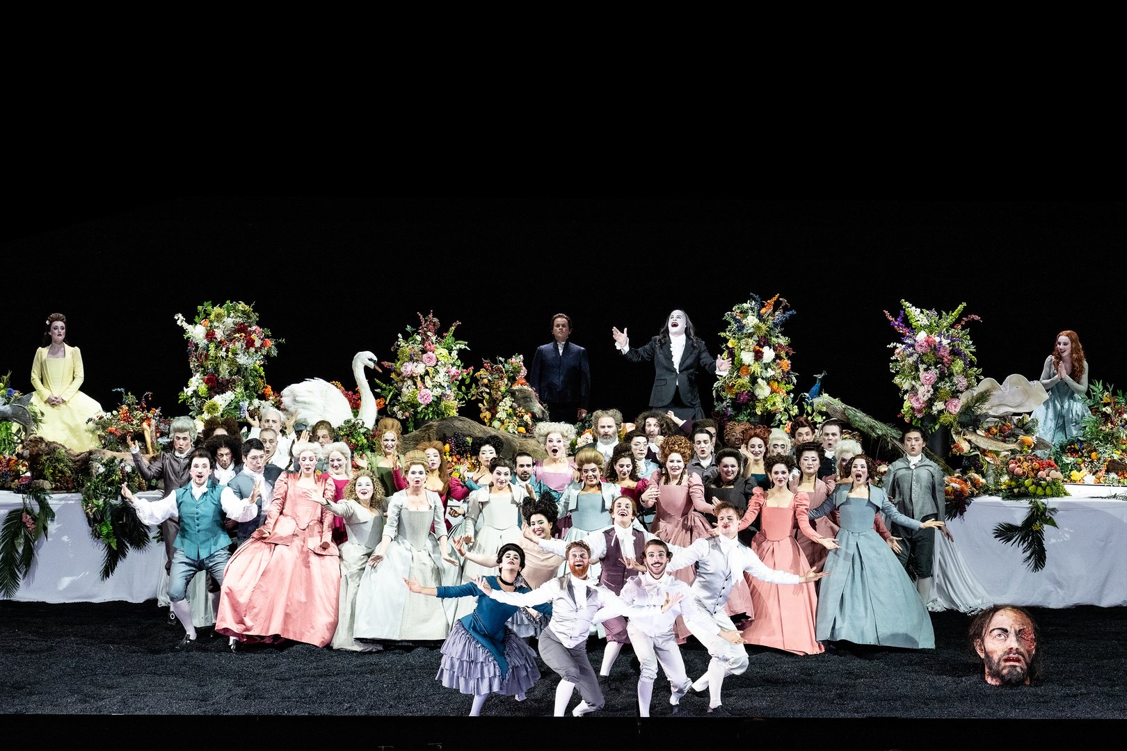 Auf dem Tisch v.l.n.r. Merab (Sarah Brady), Jonathan (Liam Bonthrone), Saul (Christopher Purves) und Michal (Giulia Montanari), davor der Chor der Oper Köln, Tänzer*innen und der Kopf Goliaths