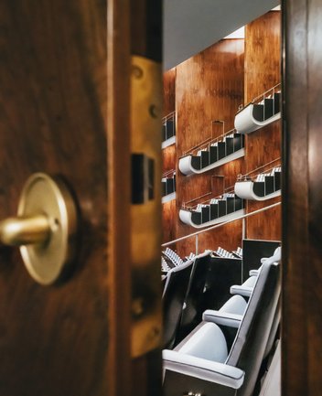 Blick durch eine leicht geöffnete Holztür in den Zuschauerraum der Oper am Offenbachplatz mit Sitzreihen mit hellblauen Bezügen und geschwungenen Balkonen vor warmen Holzvertäfelungen.