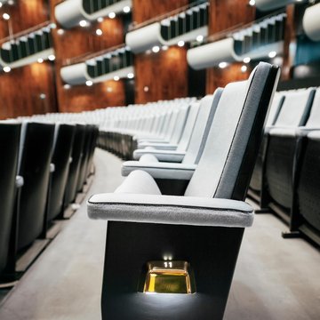 Seitliche Nahaufnahme einer Sitzreihe im Opernsaal der Oper Köln am Offenbachplatz mit gepolsterten Sitzen und integrierten Platznummern. Die Perspektive entlang der Reihe betont die Tiefe des Raums und die hochwertige Ausstattung.