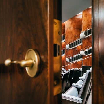 Durch eine leicht geöffnete Tür fällt der Blick in den Zuschauerraum der Oper Köln am Offenbachplatz. Im Vordergrund ist die Tür mit Griff zu sehen, dahinter öffnen sich gestaffelte Sitzreihen und Ränge, die die Tiefe und Architektur des Saals erahnen lassen.