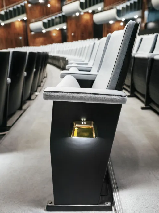 Seitliche Nahaufnahme einer Sitzreihe im Opernsaal der Oper Köln am Offenbachplatz mit gepolsterten Sitzen und integrierten Platznummern. Die Perspektive entlang der Reihe betont die Tiefe des Raums und die hochwertige Ausstattung.