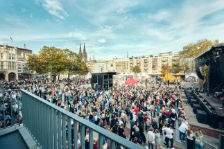 Eine große Menschenmenge versammelt sich beim Eröffnungsfest der Bühnen Köln vor der Bühne auf dem Offenbachplatz. Im Hintergrund sind die Türme des Kölner Doms zu sehen.