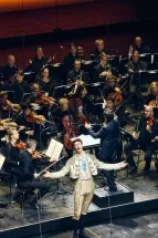 Wolfgang Stefan Schwaiger singt mit ausgebreiteten Armen vor dem Gürzenich-Orchester Köln. Hinter ihm dirigiert GMD Andrés Orozco-Estrada.