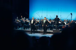 Young Woo Kim und Insik Choi singen an Mikrofonen vor dem Gürzenich-Orchester Köln. Hinter ihnen dirigiert GMD Andrés Orozco-Estrada.