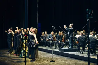 Wolfgang Stefan Schwaiger, Insik Choi, Sabine Heinrich, Laura Kriese, Adriana Bastidas-Gamboa, Young Woo Kim und Emily Hindrichs stehen mit erhobenen Armen auf der Bühne. Andrés Orozco-Estrada applaudiert am Dirigentenpult; hinter ihm sitzt das Gürzenich-Orchester Köln.