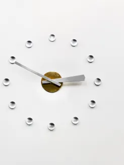 Minimalist wall clock in the Opera House at Offenbachplatz with silver hands, a gold center, and twelve glass dots marking the hours on a white background.