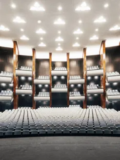 Blick von der Bühne in den Zuschauerraum der Oper am Offenbachplatz mit ansteigenden Sitzreihen mit hellblauen Bezügen, mehreren geschwungenen Balkonen und warmen Holzvertäfelungen.