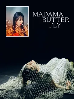 Plakat für den Theaterworkshop Madama Butterfly. Vor einer dunklen Bühnenkulisse liegt eine Person in weißer Kleidung am Boden, umgeben von einem grobmaschigen Netz im Vordergrund. Mit geschlossenen Augen blickt sie nach oben. Im oberen linken Bereich ist ein gerahmtes Porträt einer Frau mit langen dunklen Haaren und rotem Lippenstift zu sehen, umgeben von blühenden Zweigen. Rechts daneben steht der Titel „Madama Butterfly“ in großer weißer Serifenschrift. Die Stimmung wirkt traumhaft und geheimnisvoll.