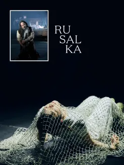 Plakat für den Theaterworkshop Madama Butterfly. Vor einer dunklen Bühnenkulisse liegt eine Person in weißer Kleidung am Boden, umgeben von einem grobmaschigen Netz im Vordergrund. Mit geschlossenen Augen blickt sie nach oben. Im oberen linken Bereich befindet sich ein gerahmtes Foto einer Opernszene: Eine kniende Person hält einen großen Fisch im Arm, während weitere Figuren im Hintergrund zu sehen sind. Rechts daneben steht der Titel „Rusalka“ in großer weißer Serifenschrift.