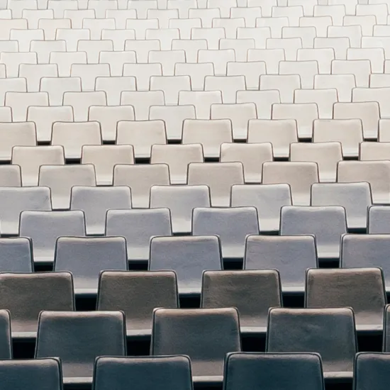 Blick auf zahlreiche, gleichmäßig angeordnete Sitzreihen im Zuschauerraum der Oper Köln am Offenbachplatz. Die hell gepolsterten Sitze bilden ein ruhiges, geometrisches Muster und vermitteln die Größe und Ordnung des Saals, während keine Personen anwesend sind.