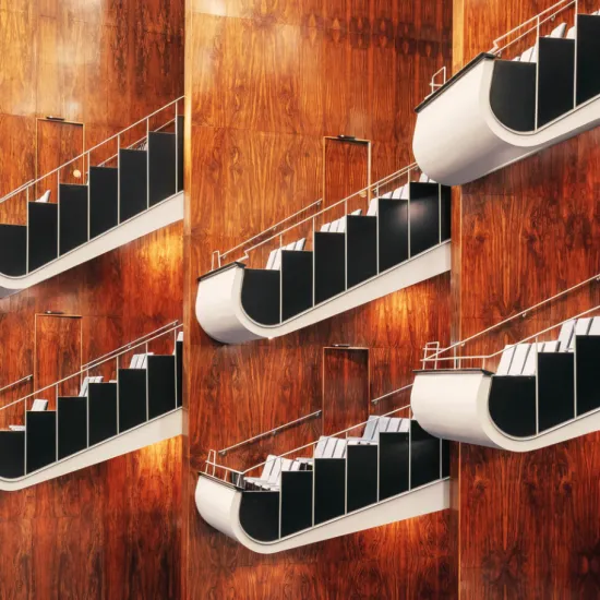 Several vertically stacked balconies of the Opera House auditorium at Oper Köln on Offenbachplatz. The curved balcony fronts, framed in white with black panels, stand out against the warm wood-panelled walls. Silver-coloured railings and the clean architectural lines create an elegant, contemporary atmosphere.