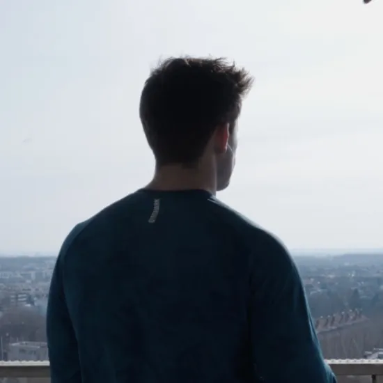 Tenor Rhydian Jenkins stands with his back to the camera, looking out over a cityscape (Cologne) beneath a cloudy sky.