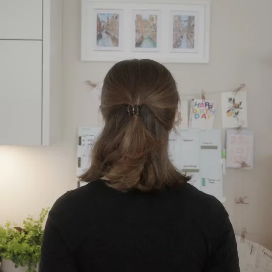 Giulia Montanari stands at home with her back to the camera, facing her wall calendar.