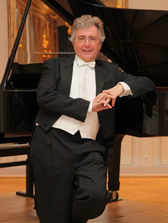 Portrait of Bernhard Steiner wearing black tails with a white bow tie and waistcoat. He smiles while leaning against an open concert grand piano.