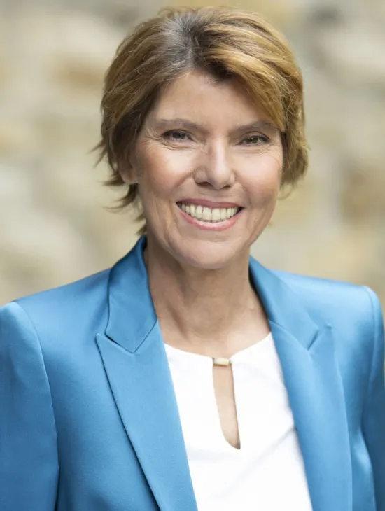 Porträt von Bettina Böttinger. Sie lächelt in die Kamera und trägt einen leuchtend blauen Blazer über einer weißen Bluse.