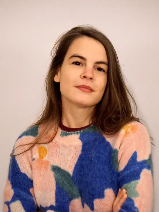 Portrait of Céline Baril against a light background. She is wearing a colourful patterned jumper and has her arms crossed.