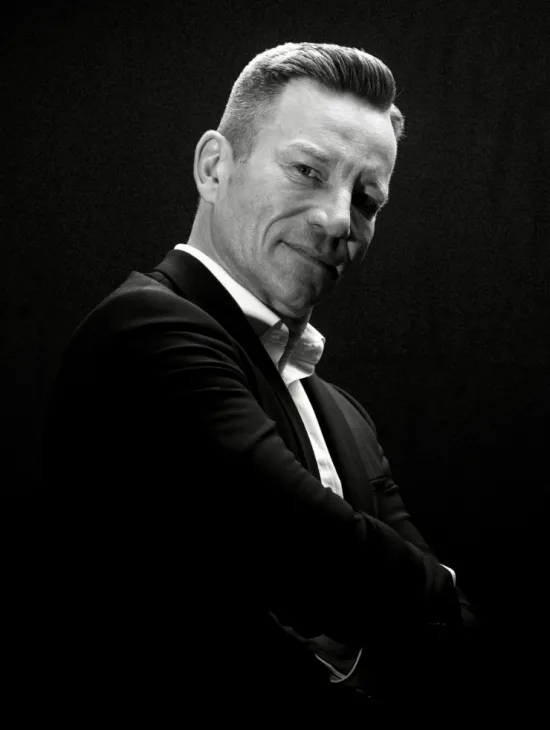 Black-and-white portrait of Jens Hermes wearing a dark suit and white shirt. He looks at the camera with a smile, his arms crossed.