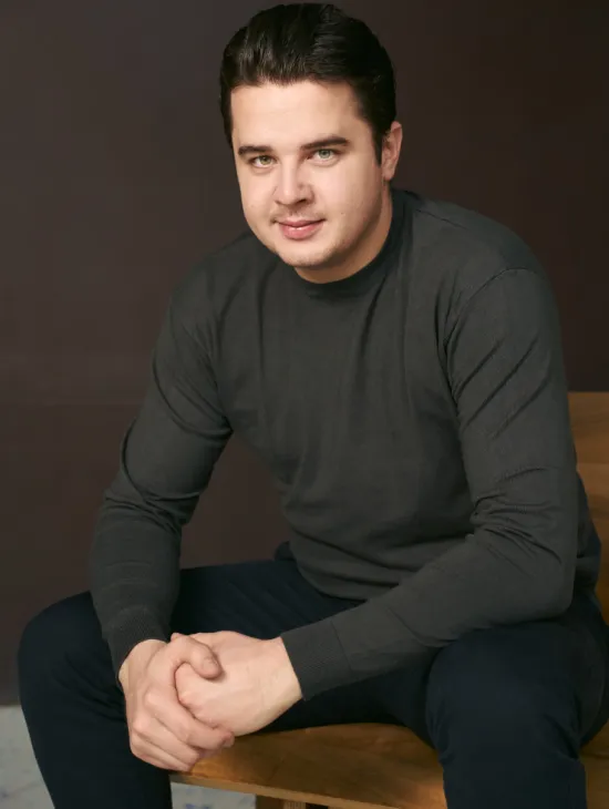Filip Filipović sitzt und blickt in die Kamera. Er trägt einen dunkelgrauen Pullover und eine dunkle Hose, die Hände sind vor ihm ineinandergelegt.