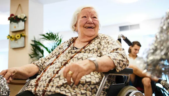 Eine ältere Teilnehmerin im Rollstuhl lacht während einer Begegnung im generationsübergreifenden Projekt Unisono. Das Projekt schafft Raum für gemeinsames Erleben, Austausch und kreative Teilhabe von Menschen verschiedener Generationen.