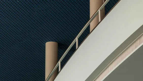 View of the foyer of the Cologne Opera at Offenbachplatz. Curved gallery levels with light-coloured balustrades and slender columns rise beneath a dark blue perforated ceiling. The architectural details emphasise the clean lines and modern design of the building.